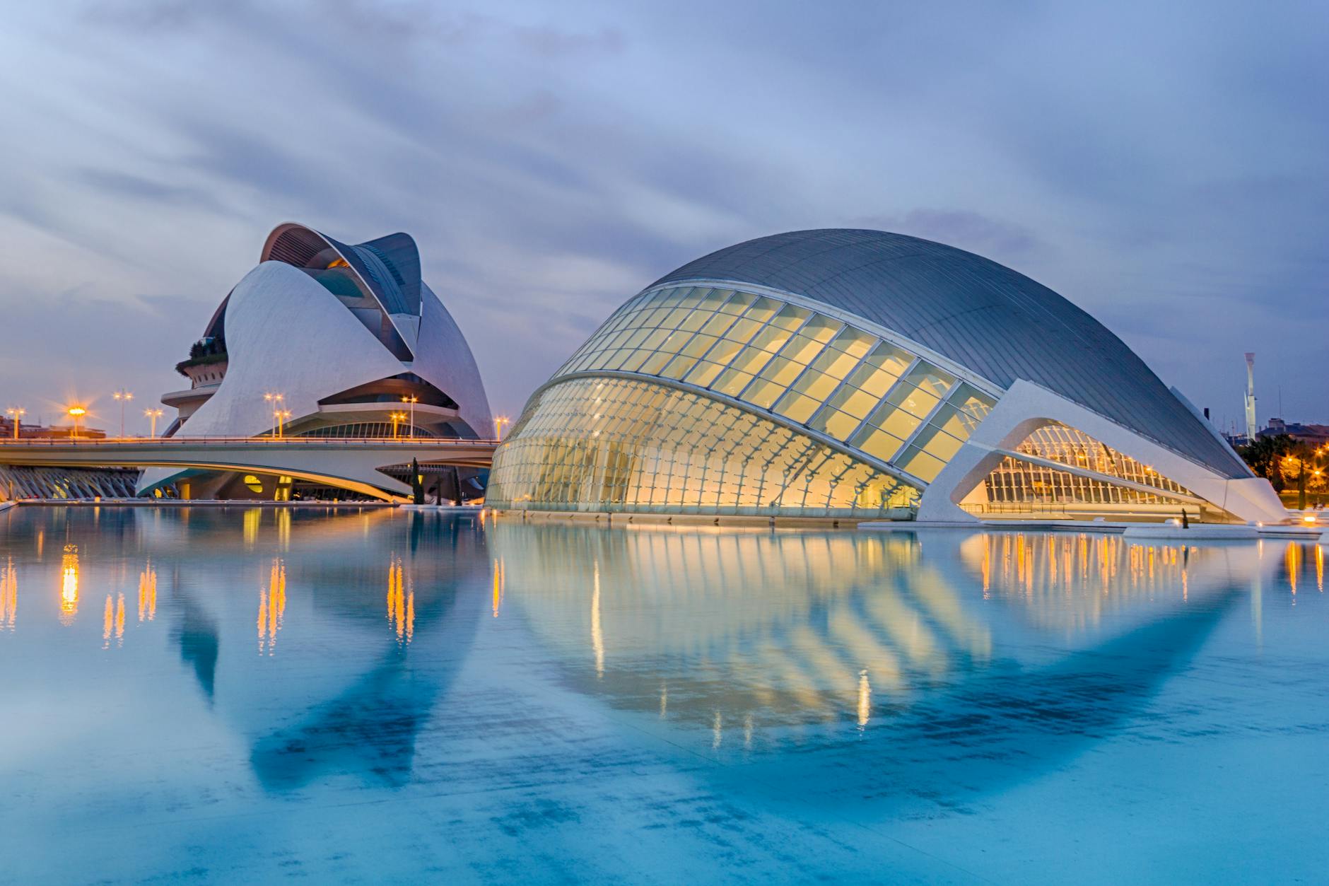 Vista de los edificios modernos de la Ciudad de las Artes y las Ciencias en Valencia, reflejados en el agua durante el atardecer.
