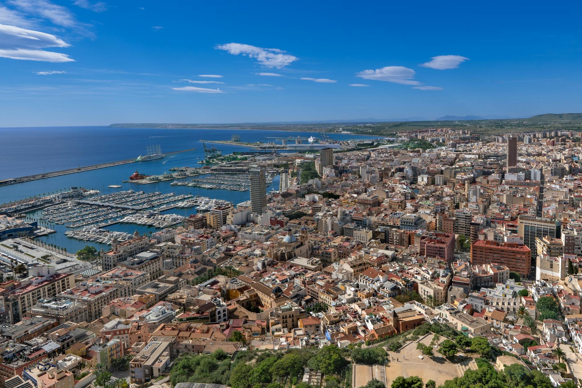 Panorámica de la costa y el puerto de Alicante, mostrando edificios y embarcaderos bajo un cielo despejado.